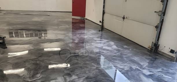 Empty garage interior with wet concrete floor, red panel on wall, and white garage door visible