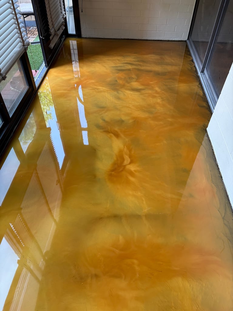 Interior room with reflective golden-brown epoxy or resin flooring, white walls, windows with blinds, and masking tape lines on the floor